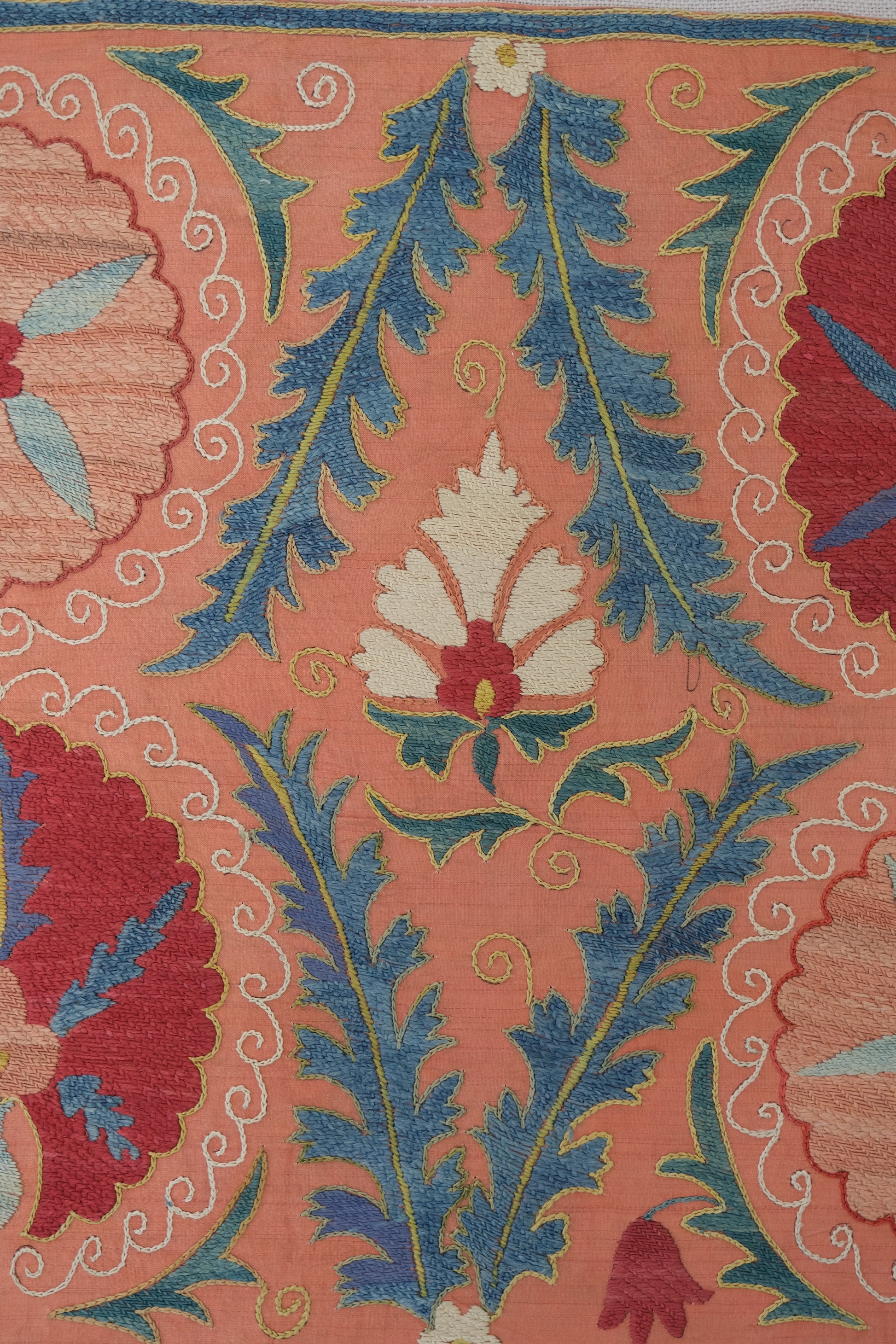Framed suzani, embroidered textile art, wooden frame, light orange with red and blue floral motifs, close-up
