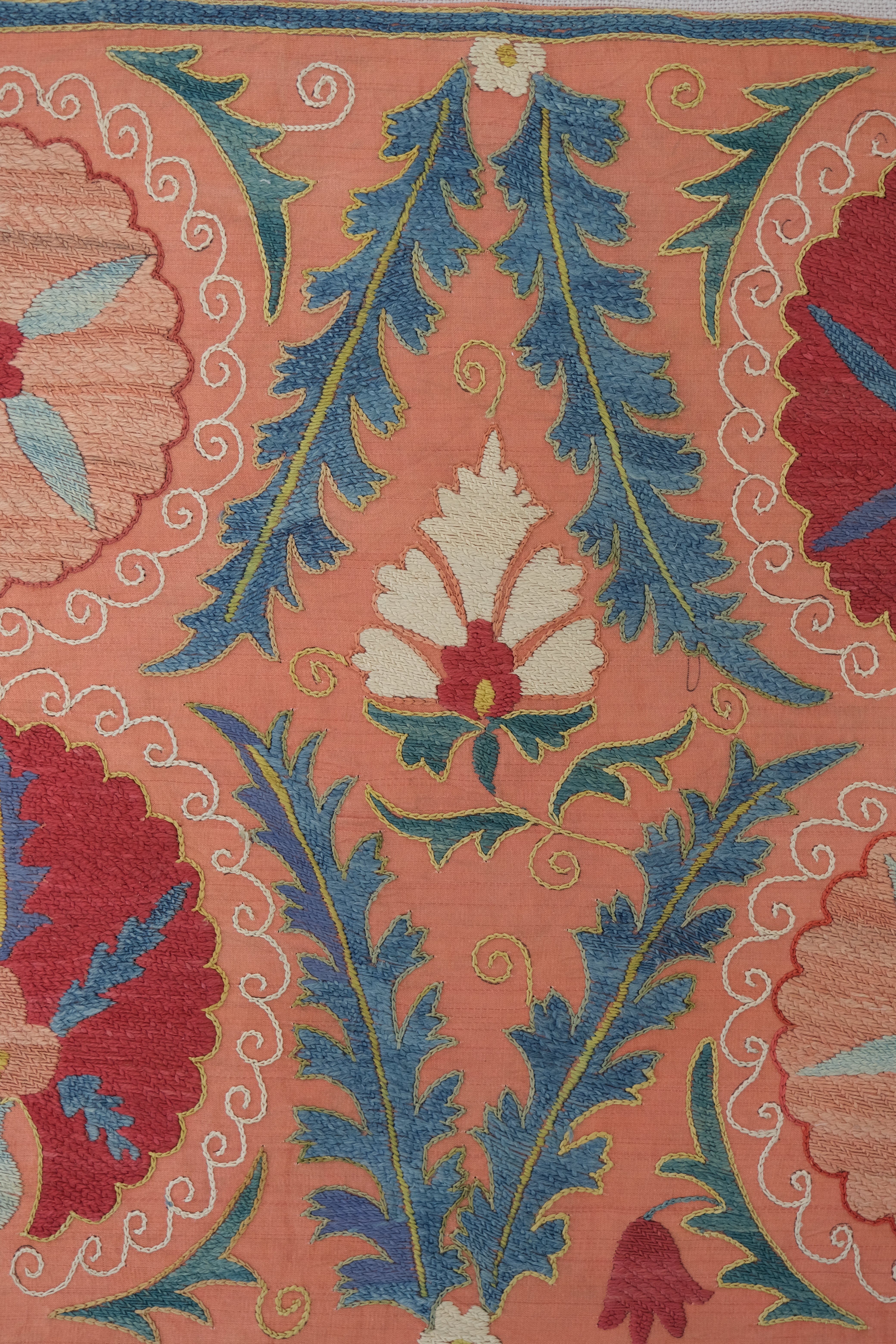 Framed suzani, embroidered textile art, wooden frame, light orange with red and blue floral motifs, close-up