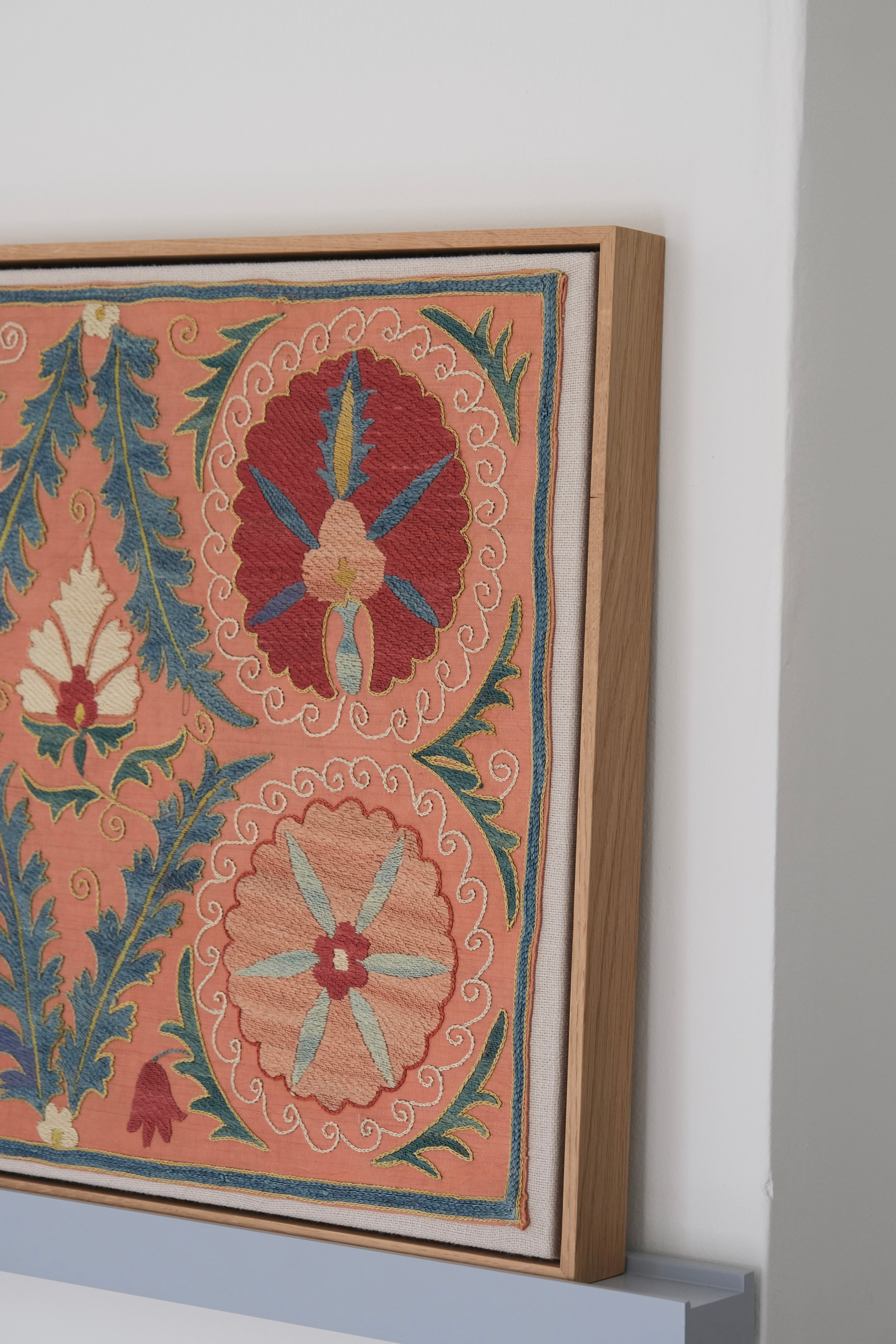 Framed suzani, embroidered textile art, wooden frame, light orange with red and blue floral motifs, side view