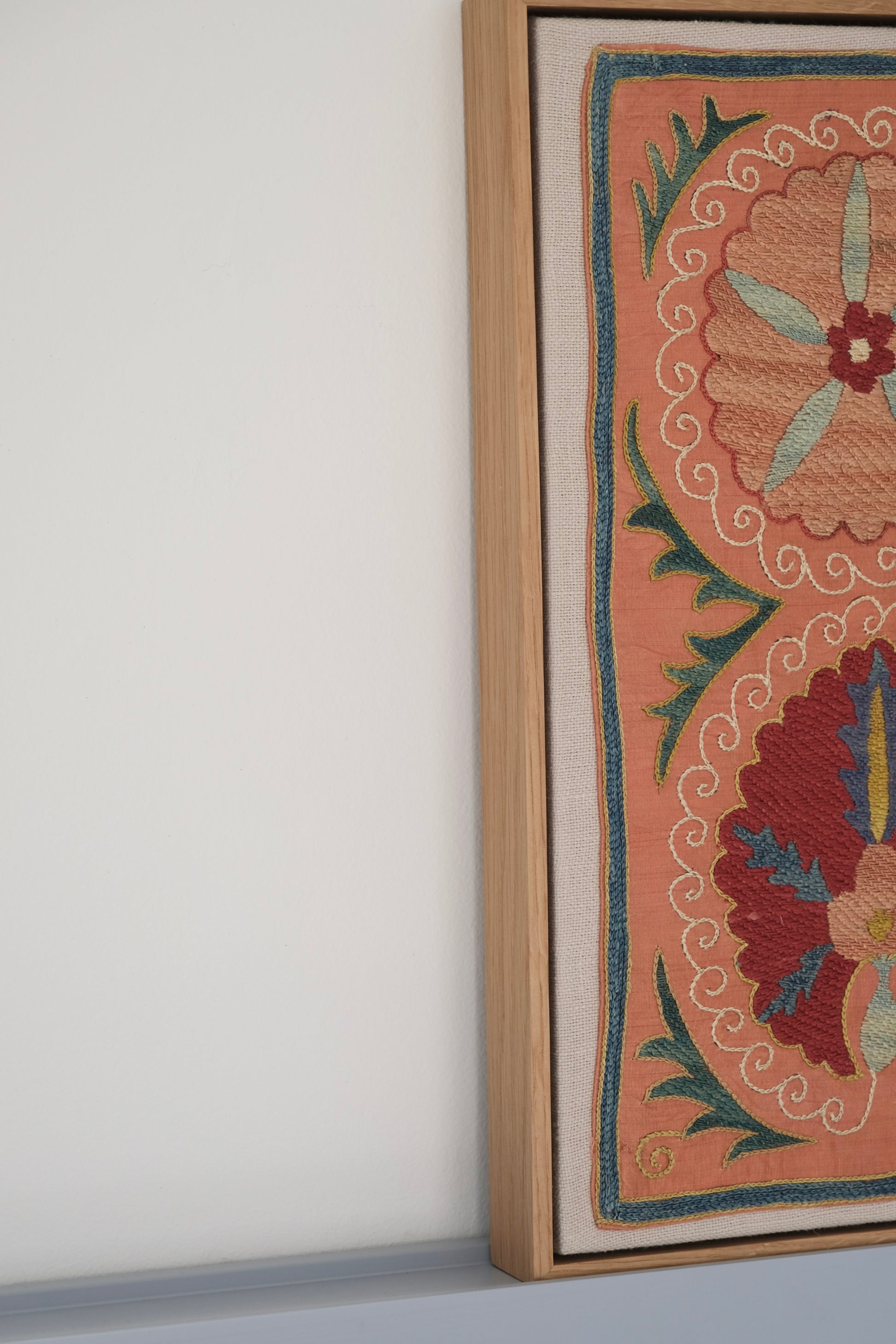 Framed suzani, embroidered textile art, wooden frame, light orange with red and blue floral motifs, side view