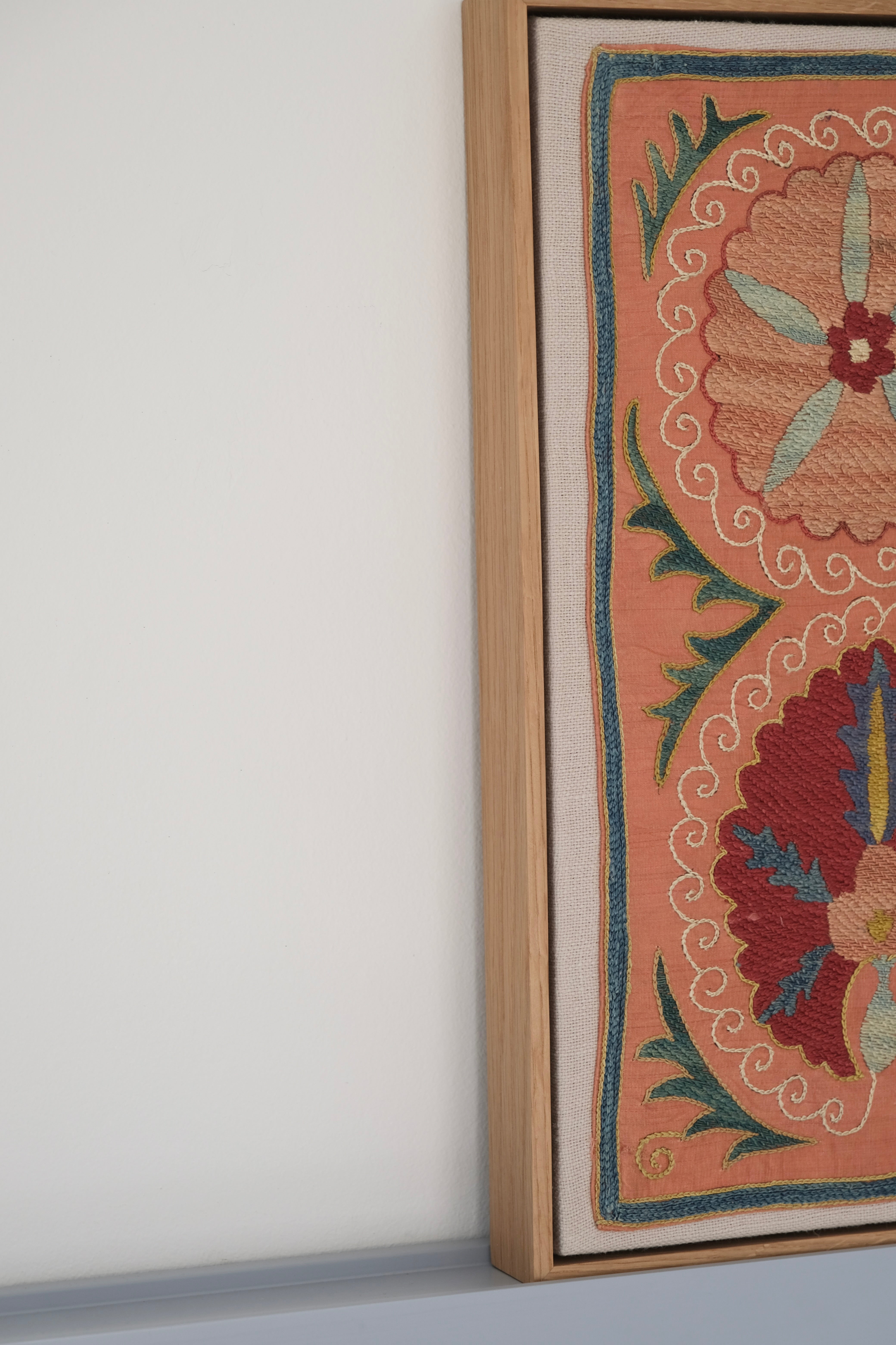 Framed suzani, embroidered textile art, wooden frame, light orange with red and blue floral motifs, side view