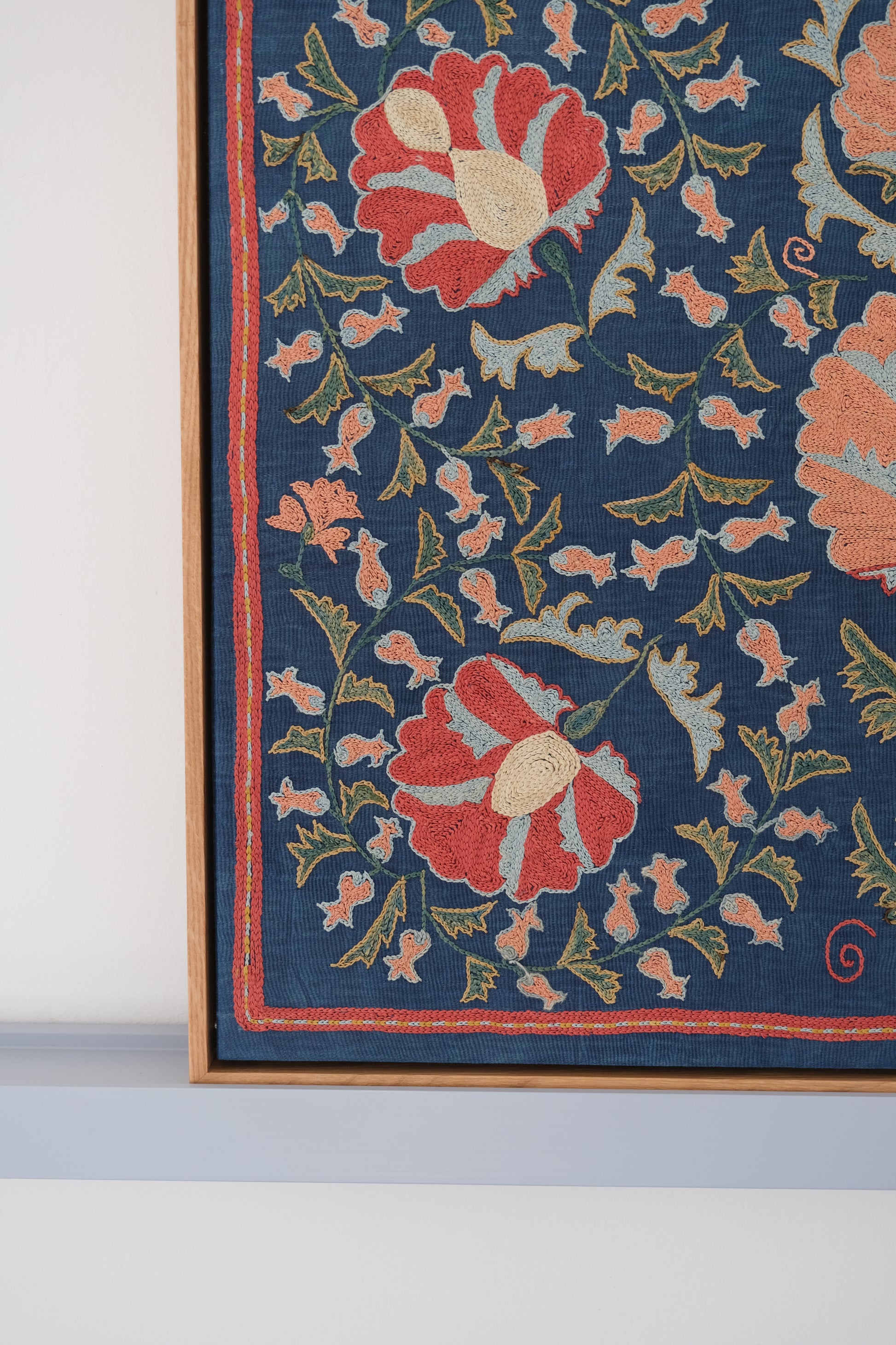Framed suzani, embroidered textile art, wooden frame, navy blue with floral motifs, close-up