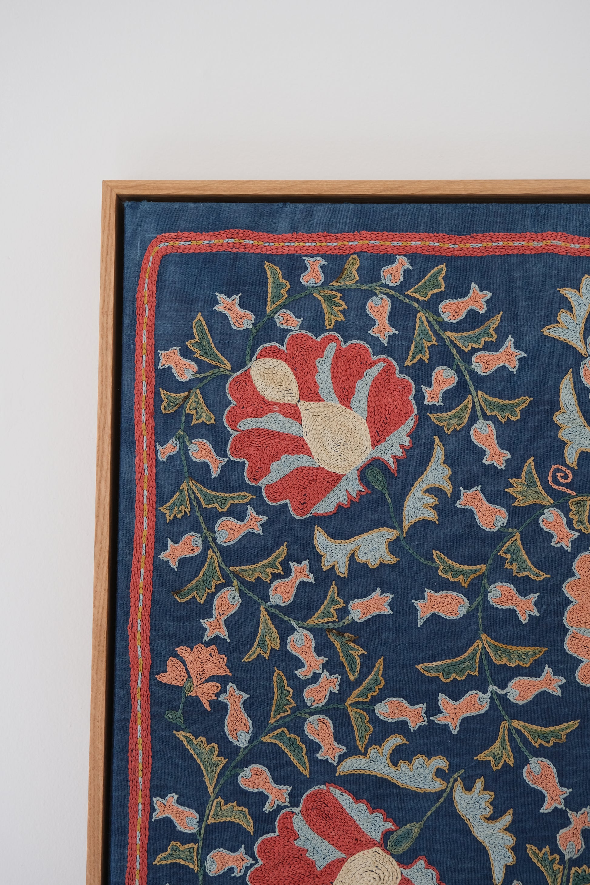 Framed suzani, embroidered textile art, wooden frame, navy blue with floral motifs, close-up