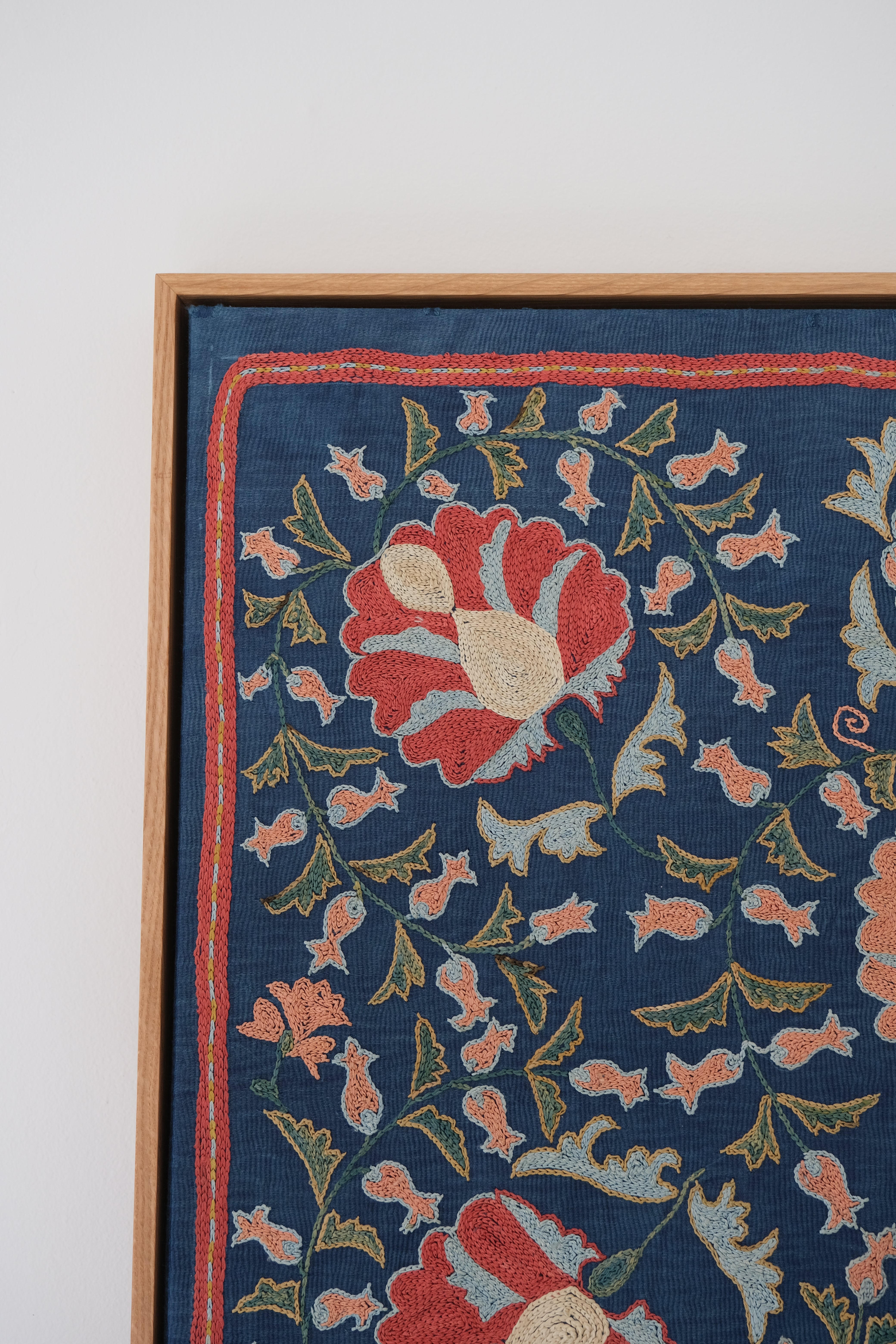 Framed suzani, embroidered textile art, wooden frame, navy blue with floral motifs, close-up
