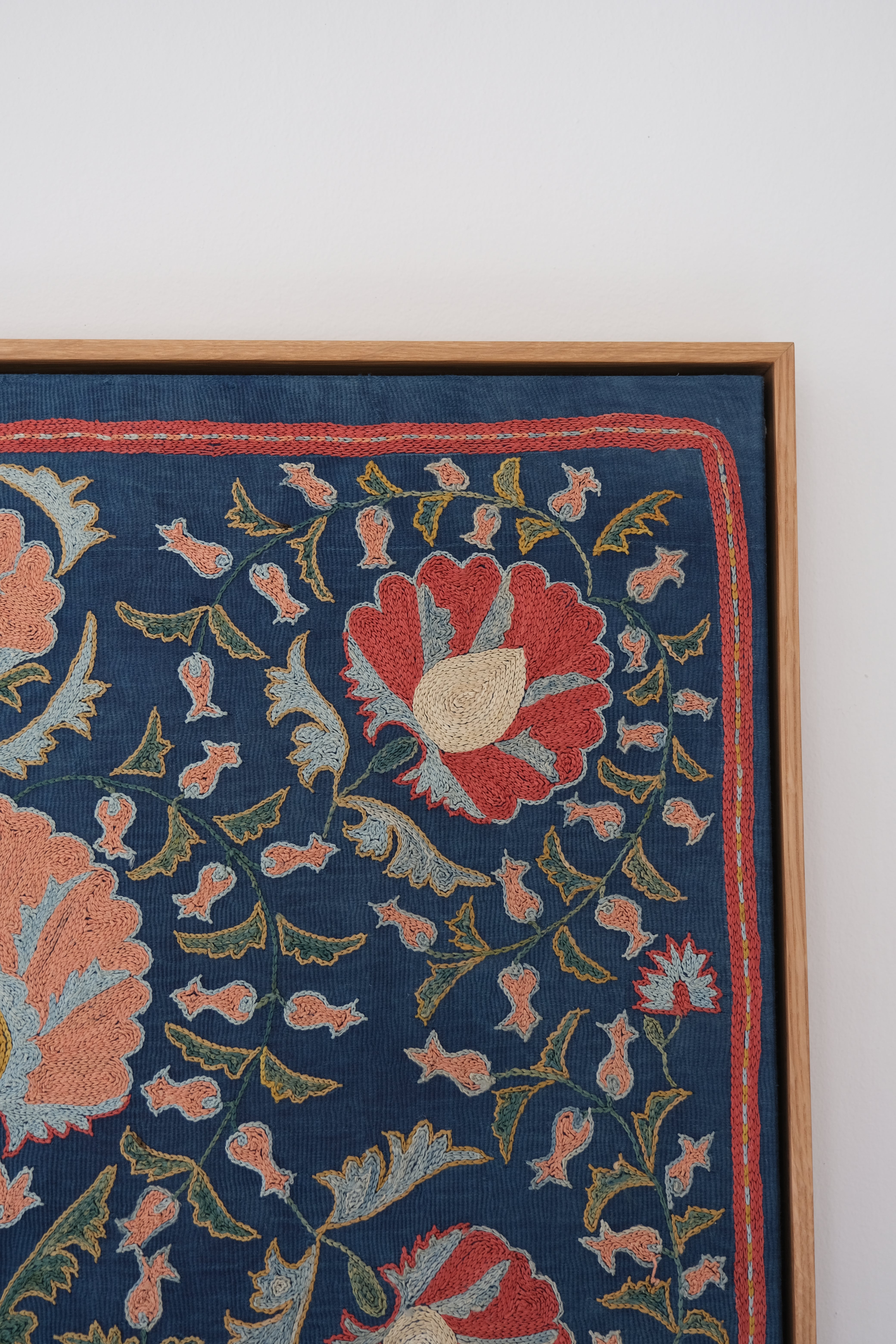 Framed suzani, embroidered textile art, wooden frame, navy blue with floral motifs, close-up