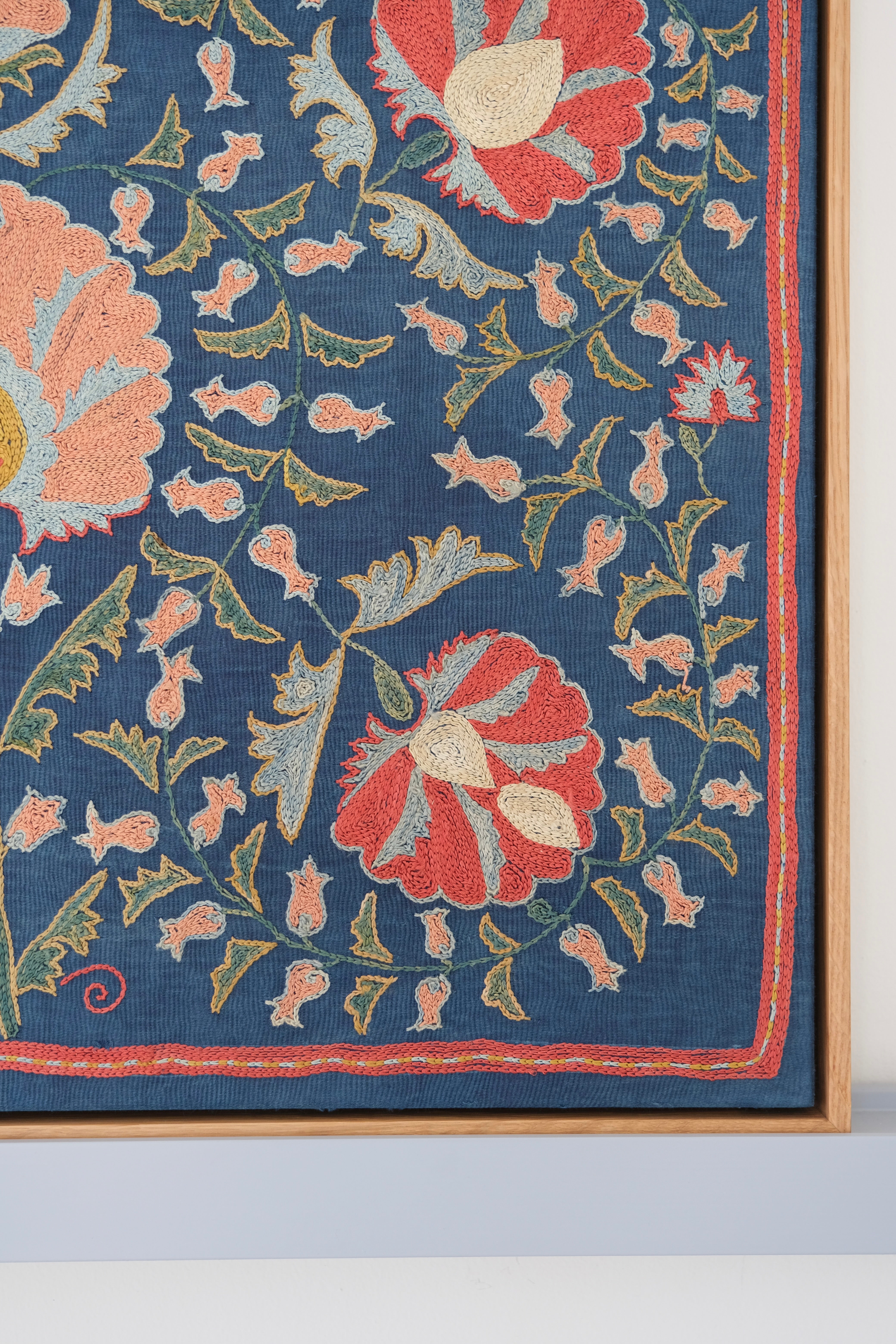 Framed suzani, embroidered textile art, wooden frame, navy blue with floral motifs, close-up