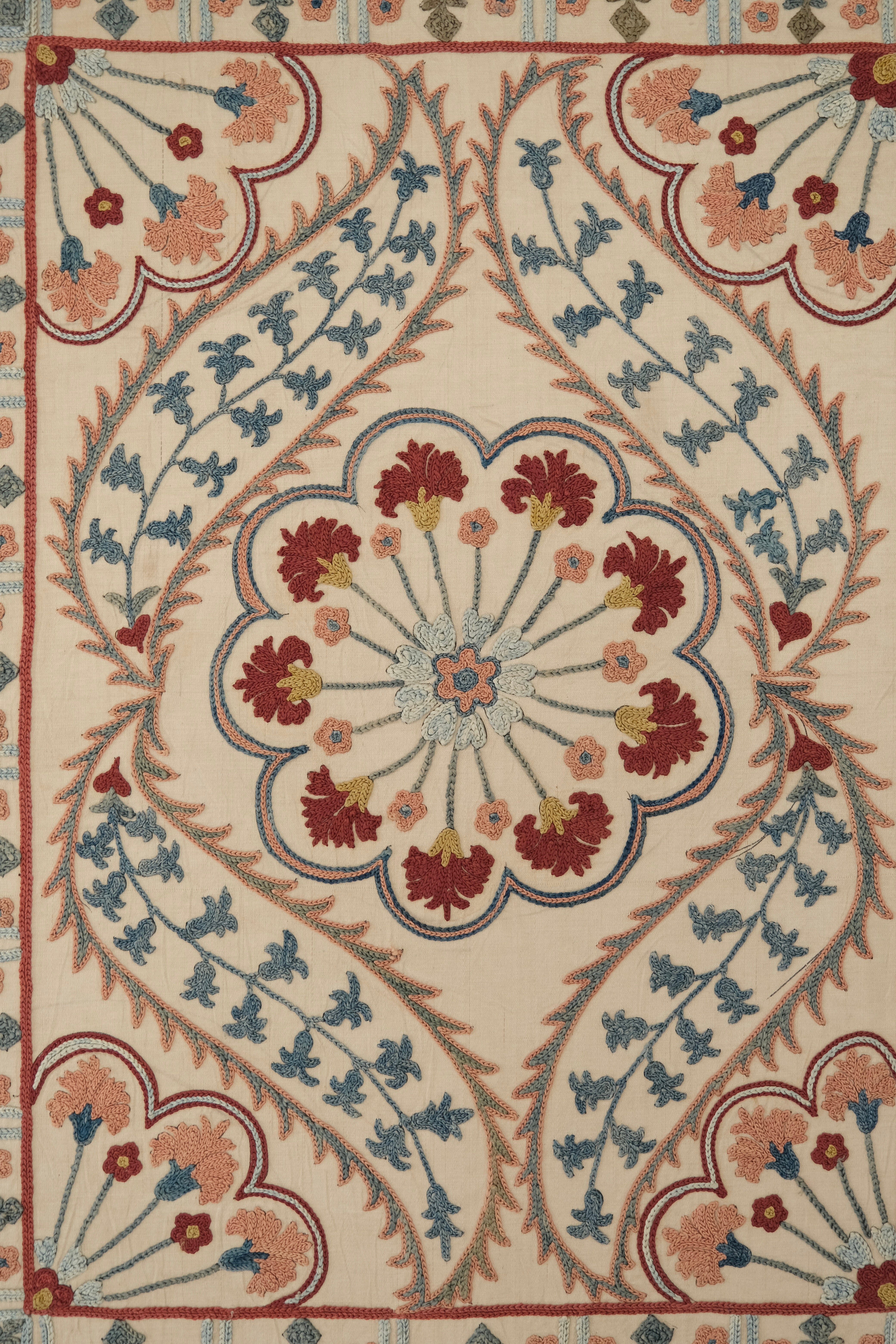 Framed suzani, embroidered textile art, wooden frame, white with blue and pink design, close-up