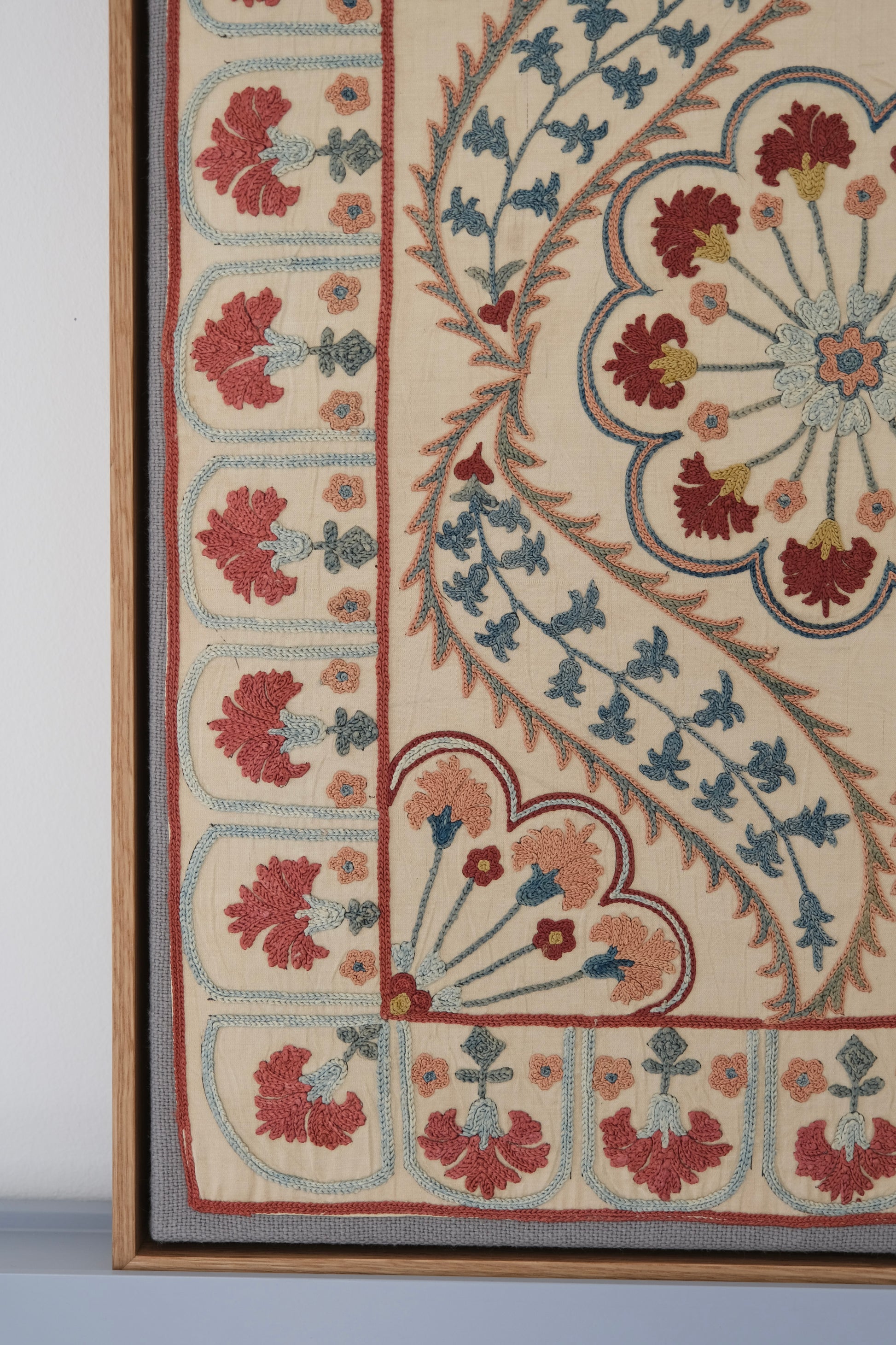 Framed suzani, embroidered textile art, wooden frame, white with blue and pink design, close-up