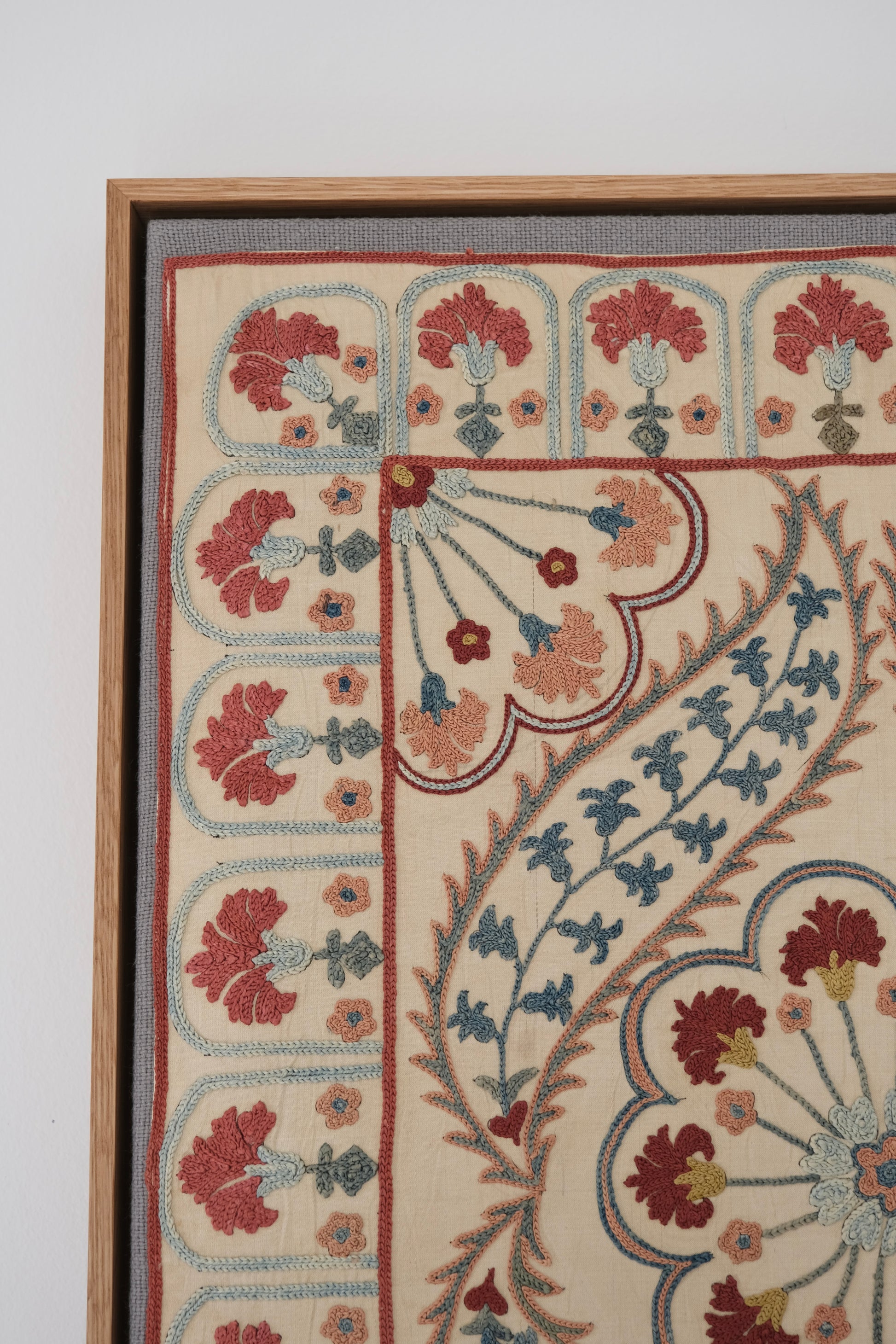 Framed suzani, embroidered textile art, wooden frame, white with blue and pink design, close-up