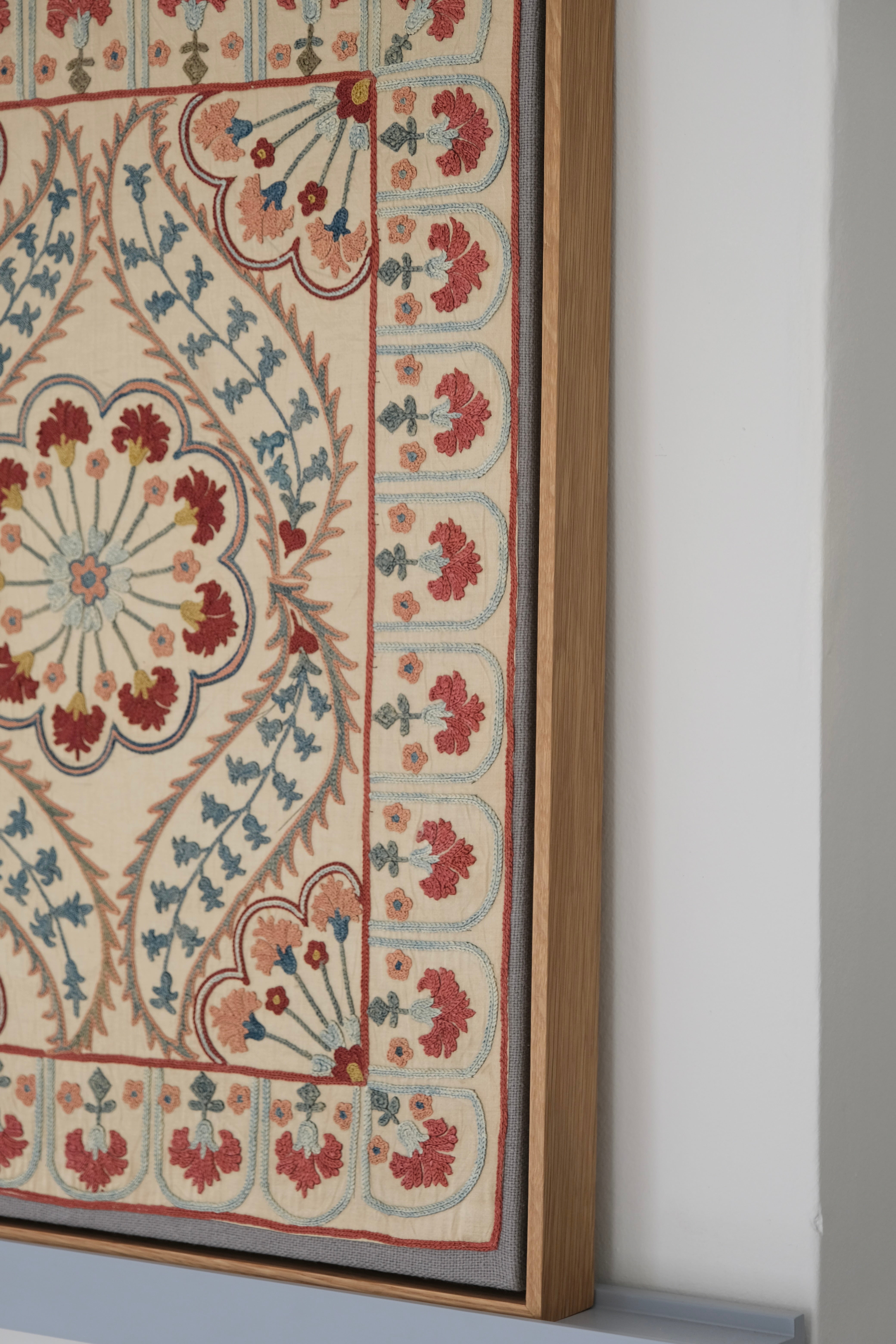 Framed suzani, embroidered textile art, wooden frame, white with blue and pink design, side view