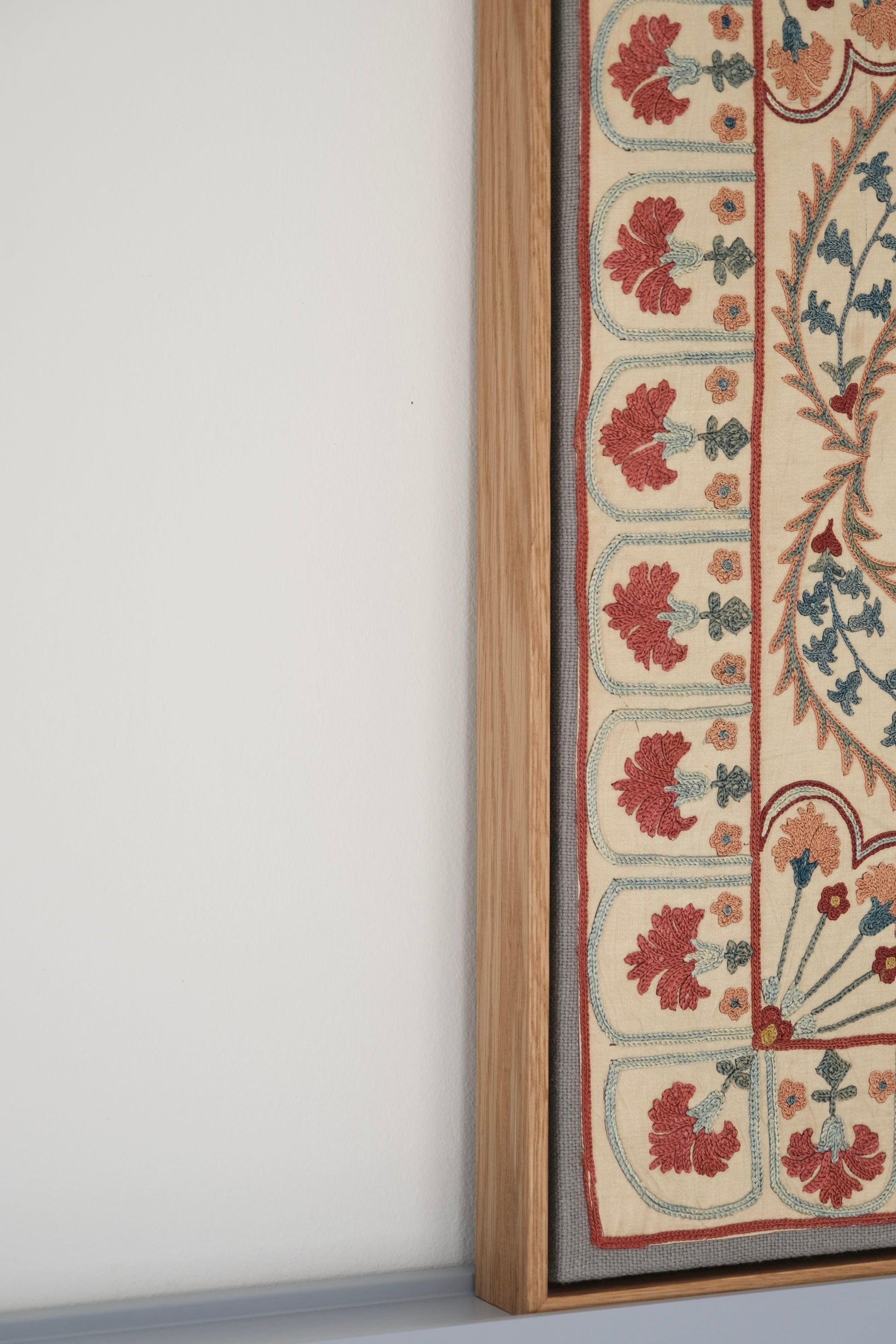 Framed suzani, embroidered textile art, wooden frame, white with blue and pink design, side view