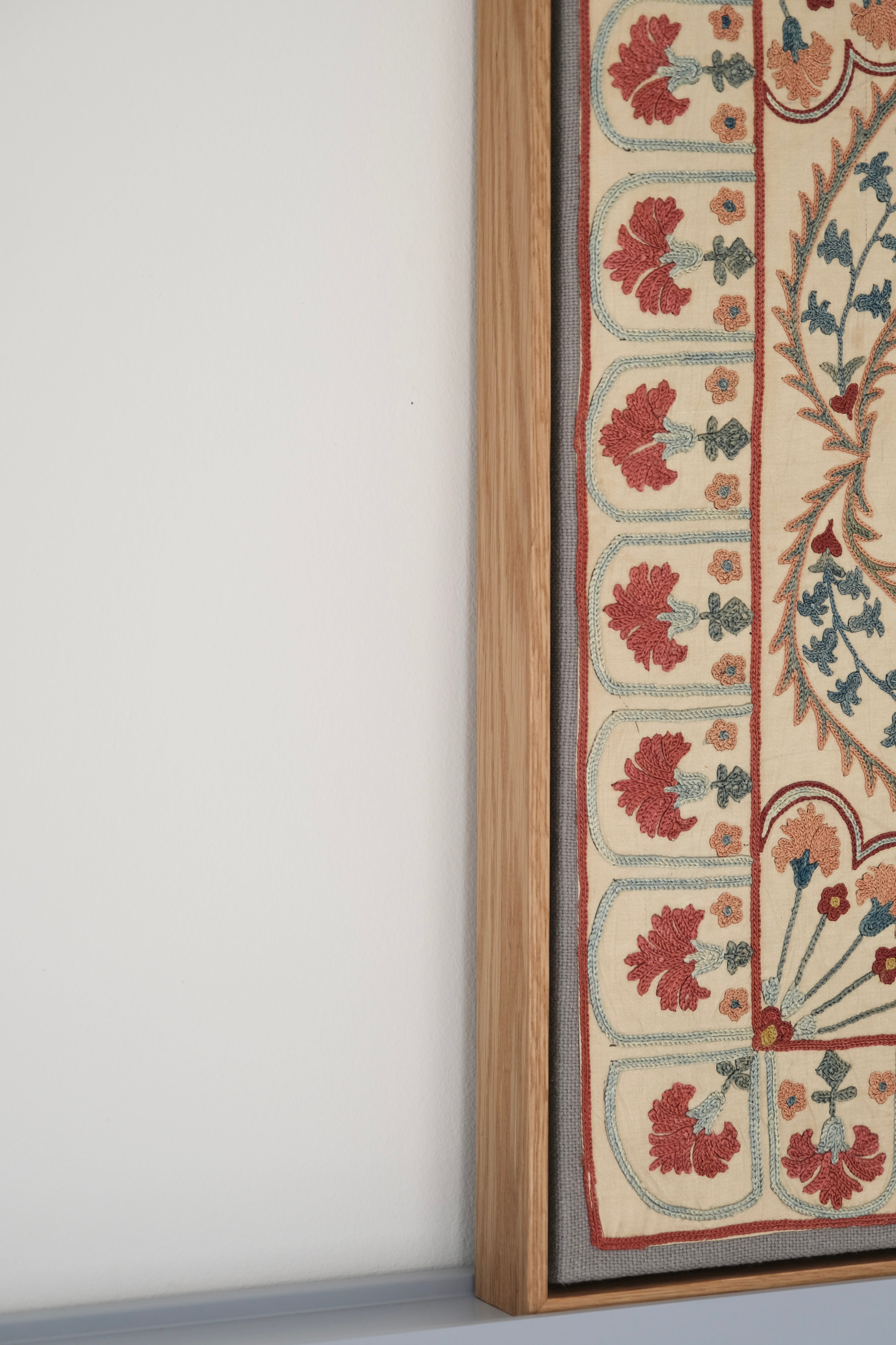 Framed suzani, embroidered textile art, wooden frame, white with blue and pink design, side view