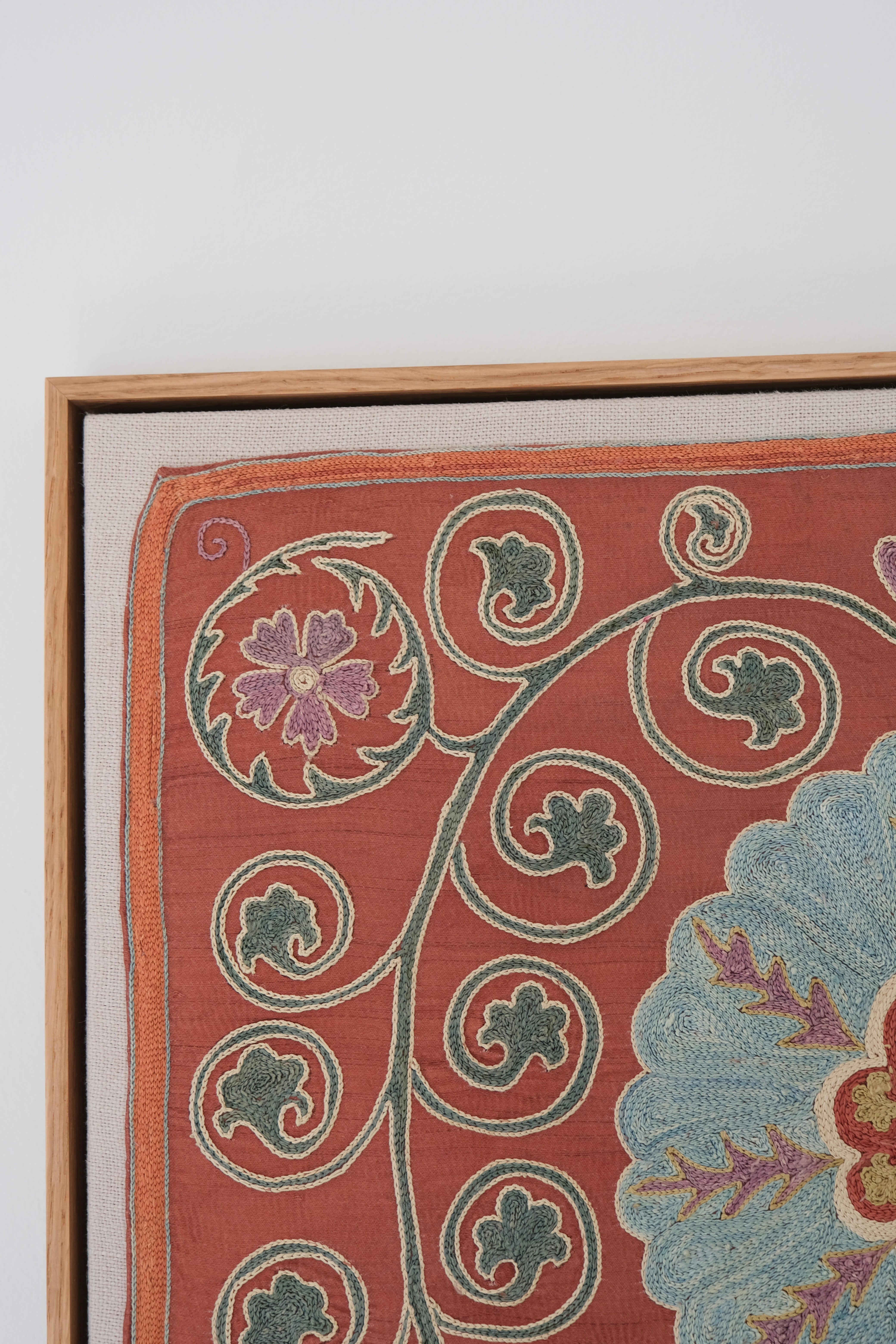 Framed suzani, embroidered textile art, wooden frame, dark orange and blue floral design, close-up