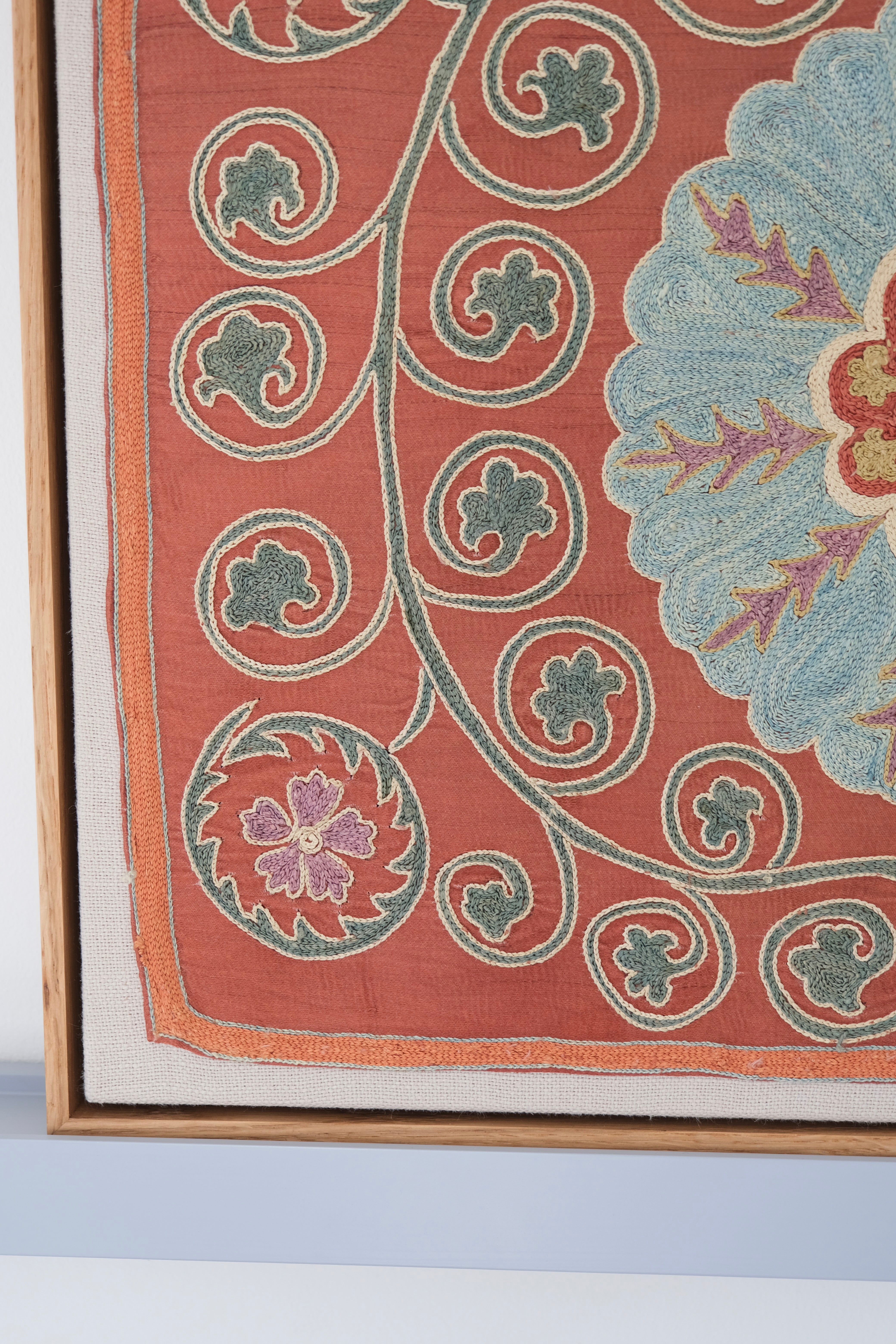 Framed suzani, embroidered textile art, wooden frame, dark orange and blue floral design, close-up