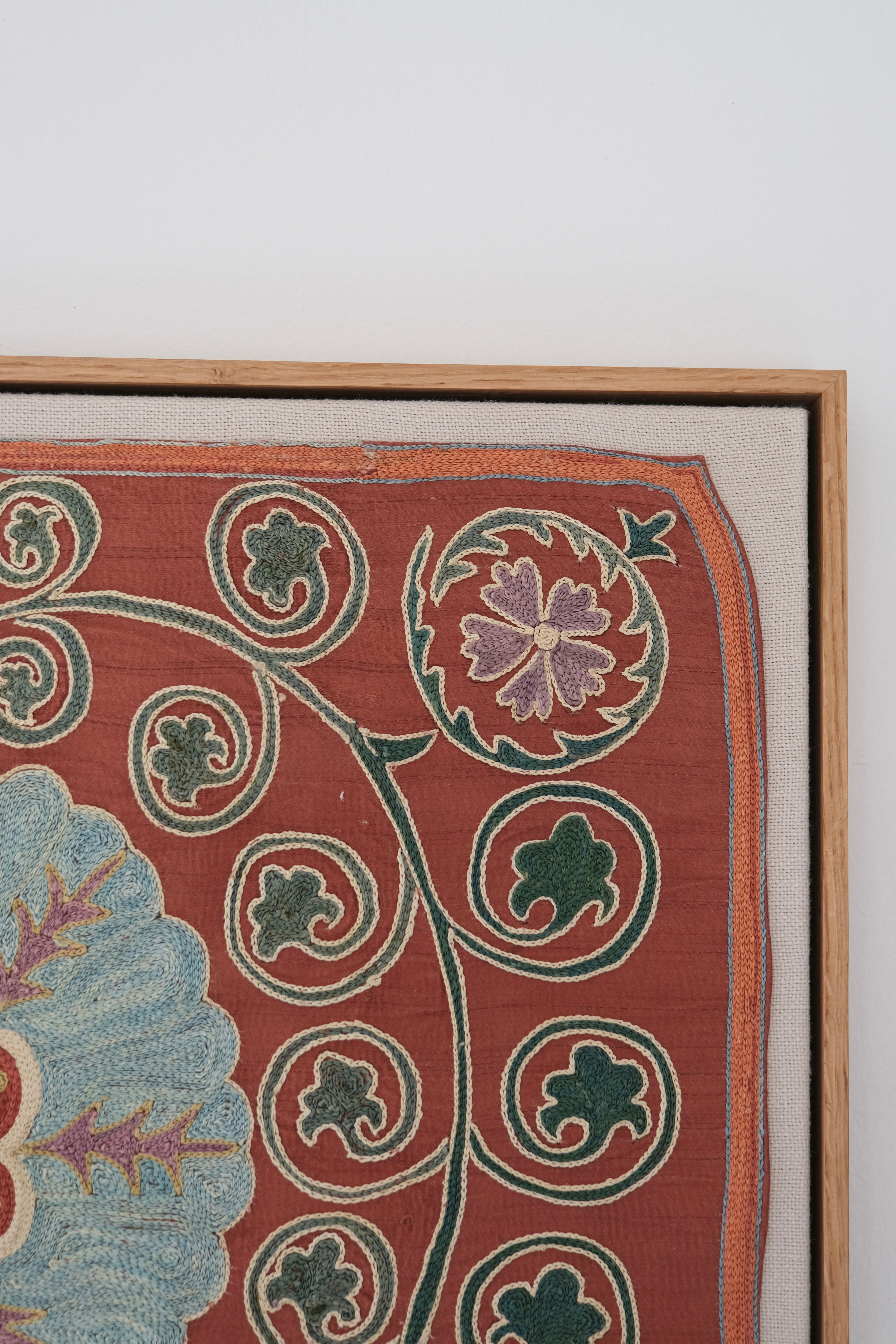 Framed suzani, embroidered textile art, wooden frame, dark orange and blue floral design, close-up