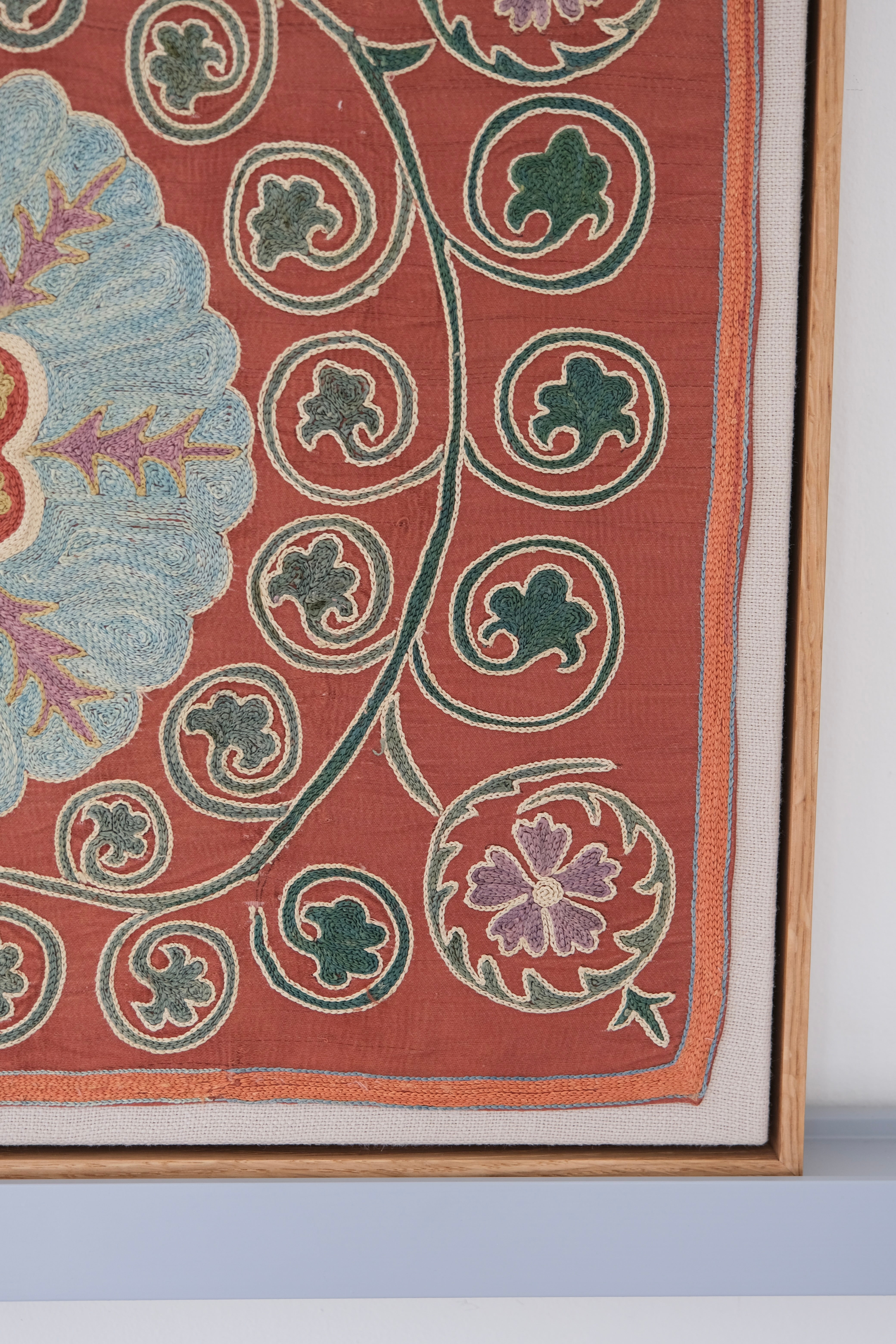 Framed suzani, embroidered textile art, wooden frame, dark orange and blue floral design, close-up