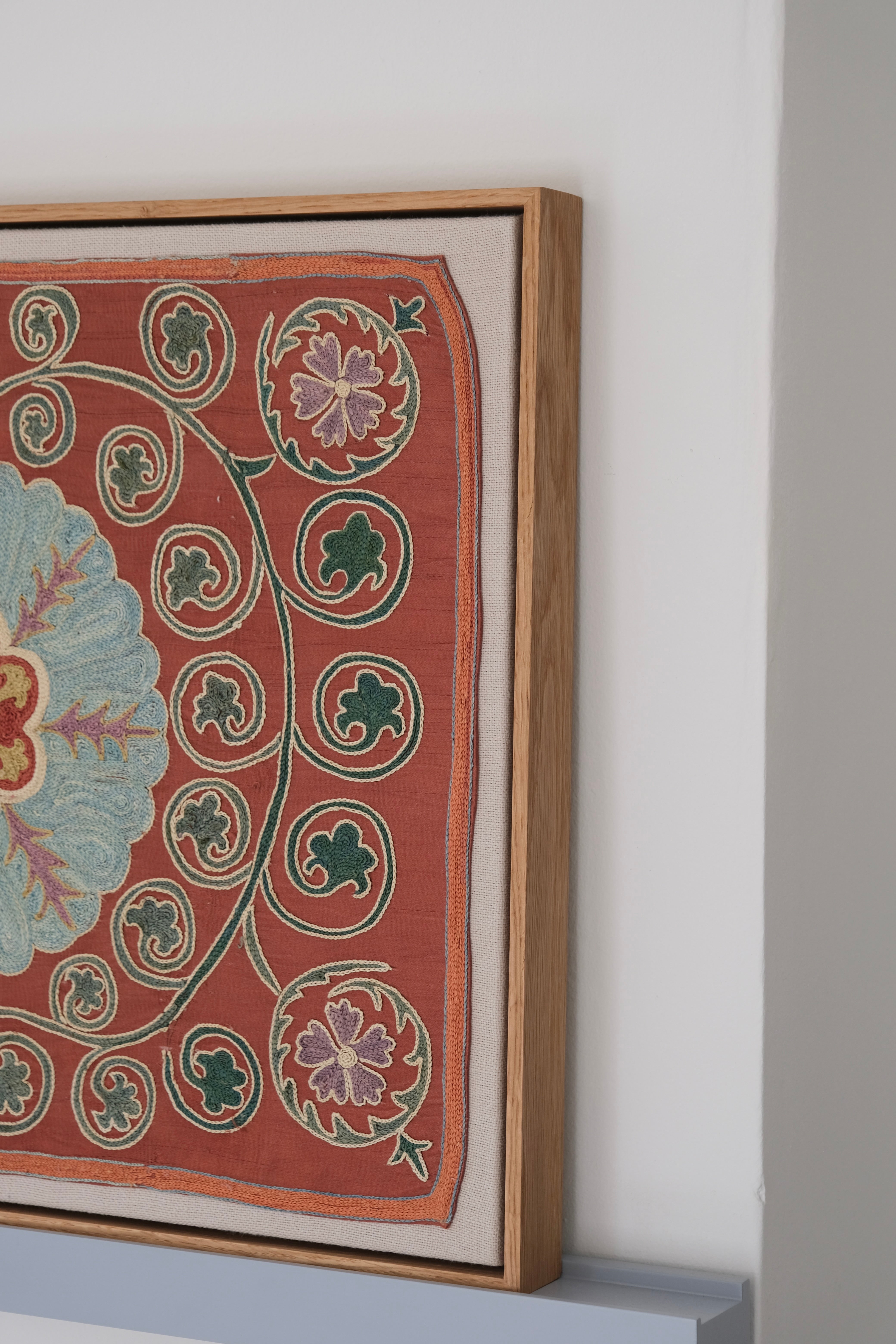 Framed suzani, embroidered textile art, wooden frame, dark orange and blue floral design, side view