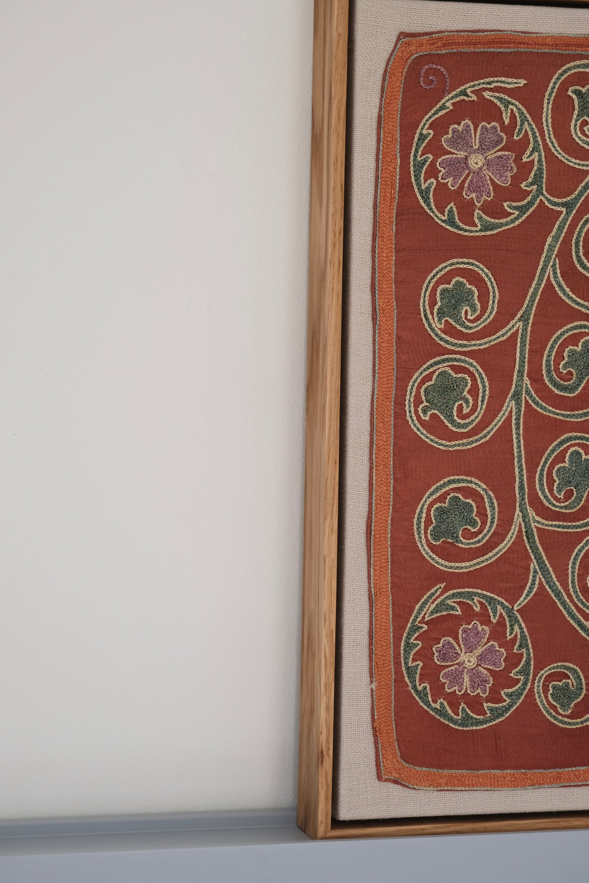 Framed suzani, embroidered textile art, wooden frame, dark orange and blue floral design, side view