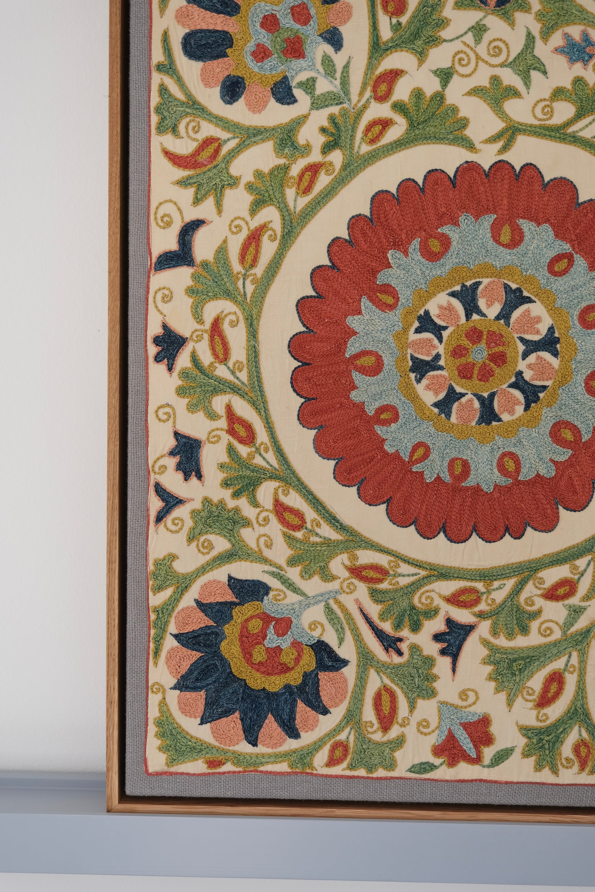 Framed suzani, embroidered textile art, wooden frame, white with green, blue and red floral design, close-up