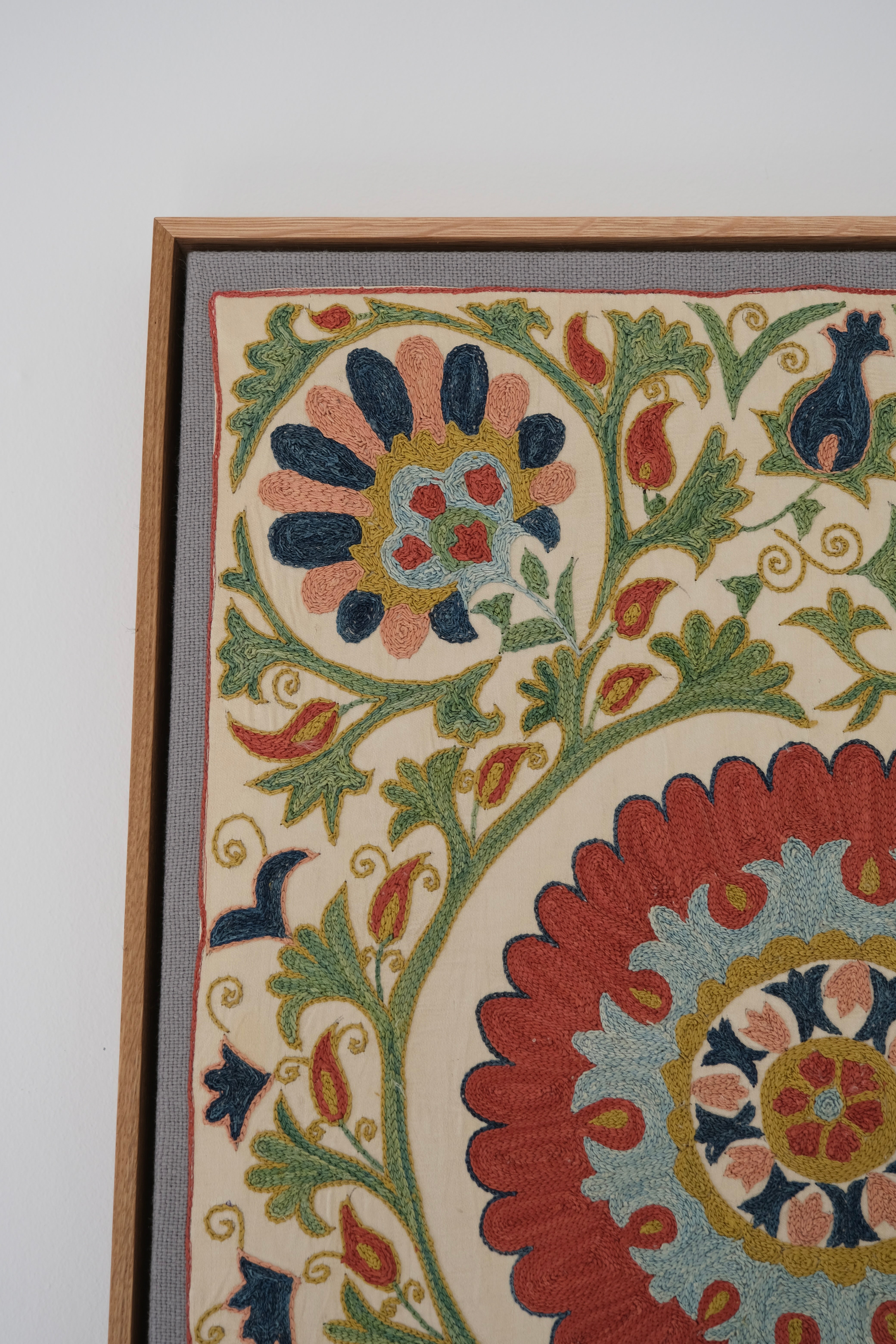 Framed suzani, embroidered textile art, wooden frame, white with green, blue and red floral design, close-up