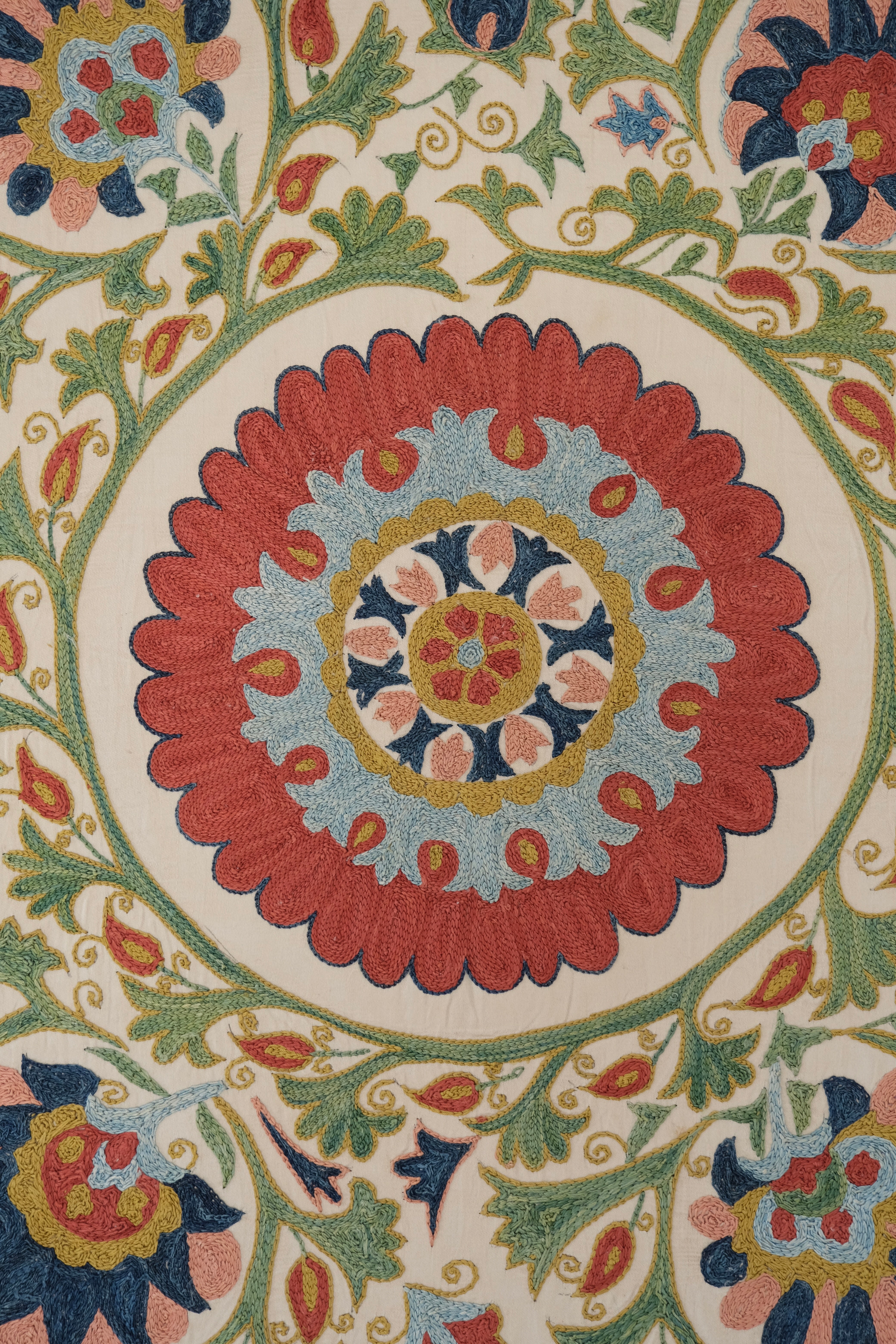 Framed suzani, embroidered textile art, wooden frame, white with green, blue and red floral design, close-up