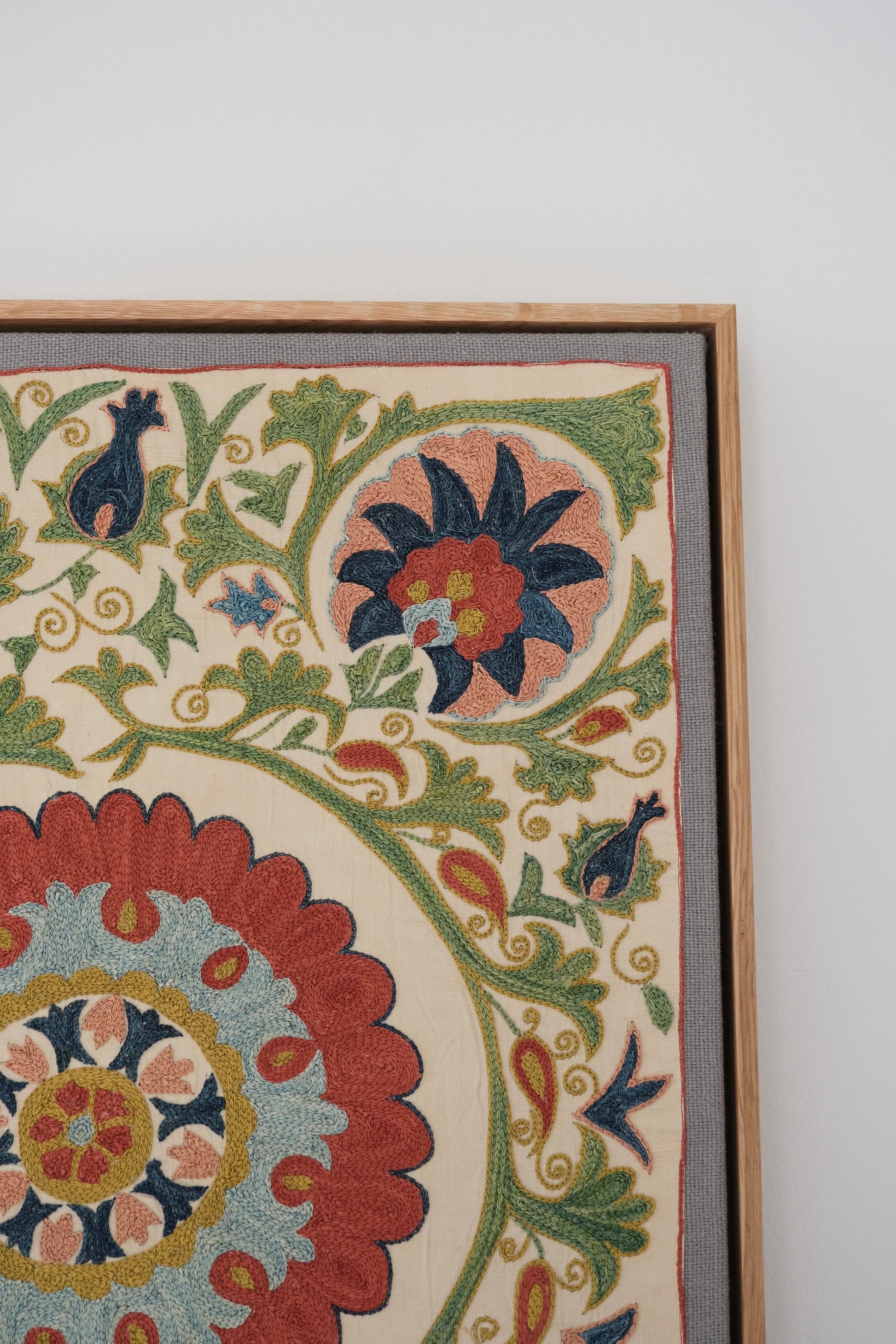 Framed suzani, embroidered textile art, wooden frame, white with green, blue and red floral design, close-up