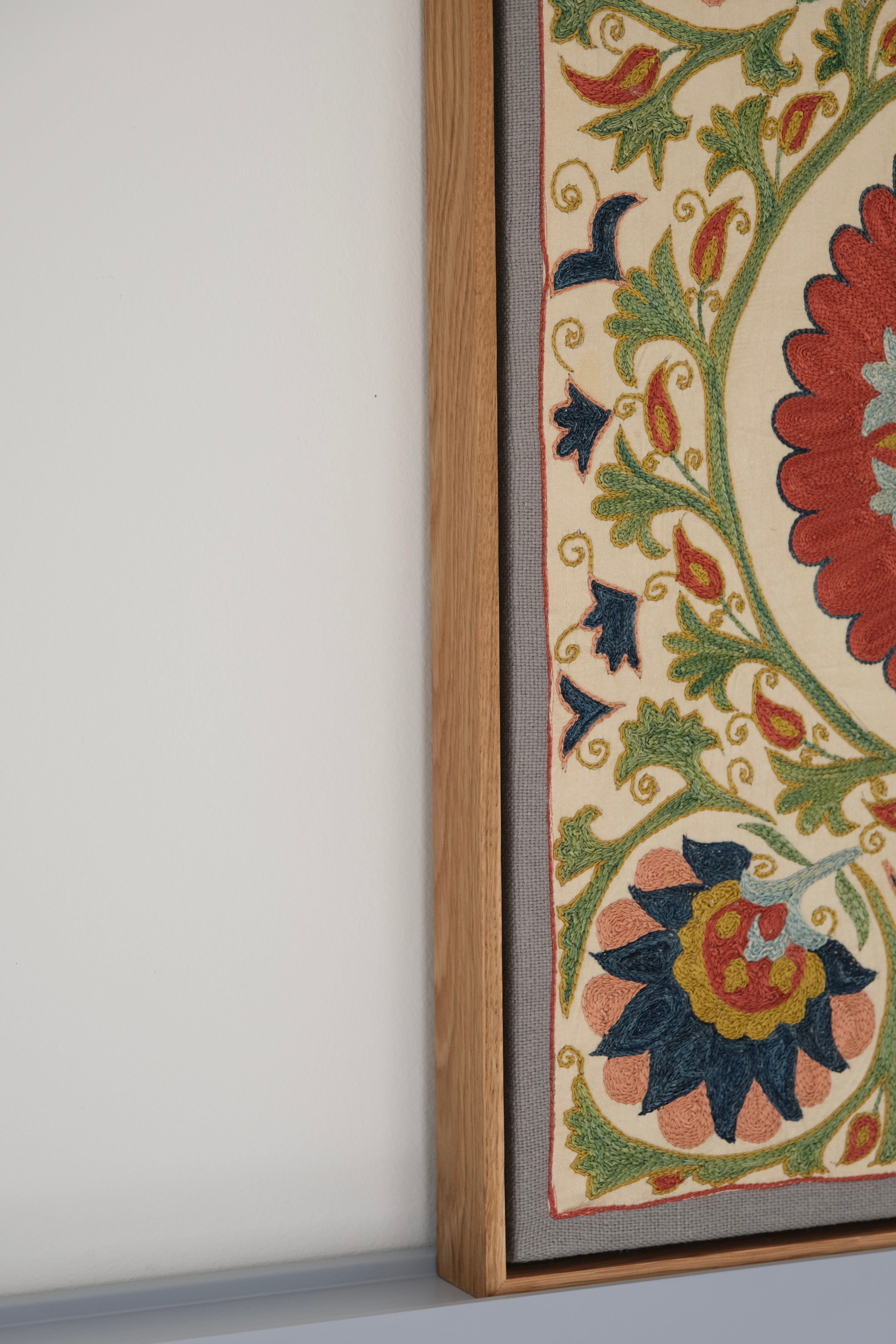 Framed suzani, embroidered textile art, wooden frame, white with green, blue and red floral design, side view