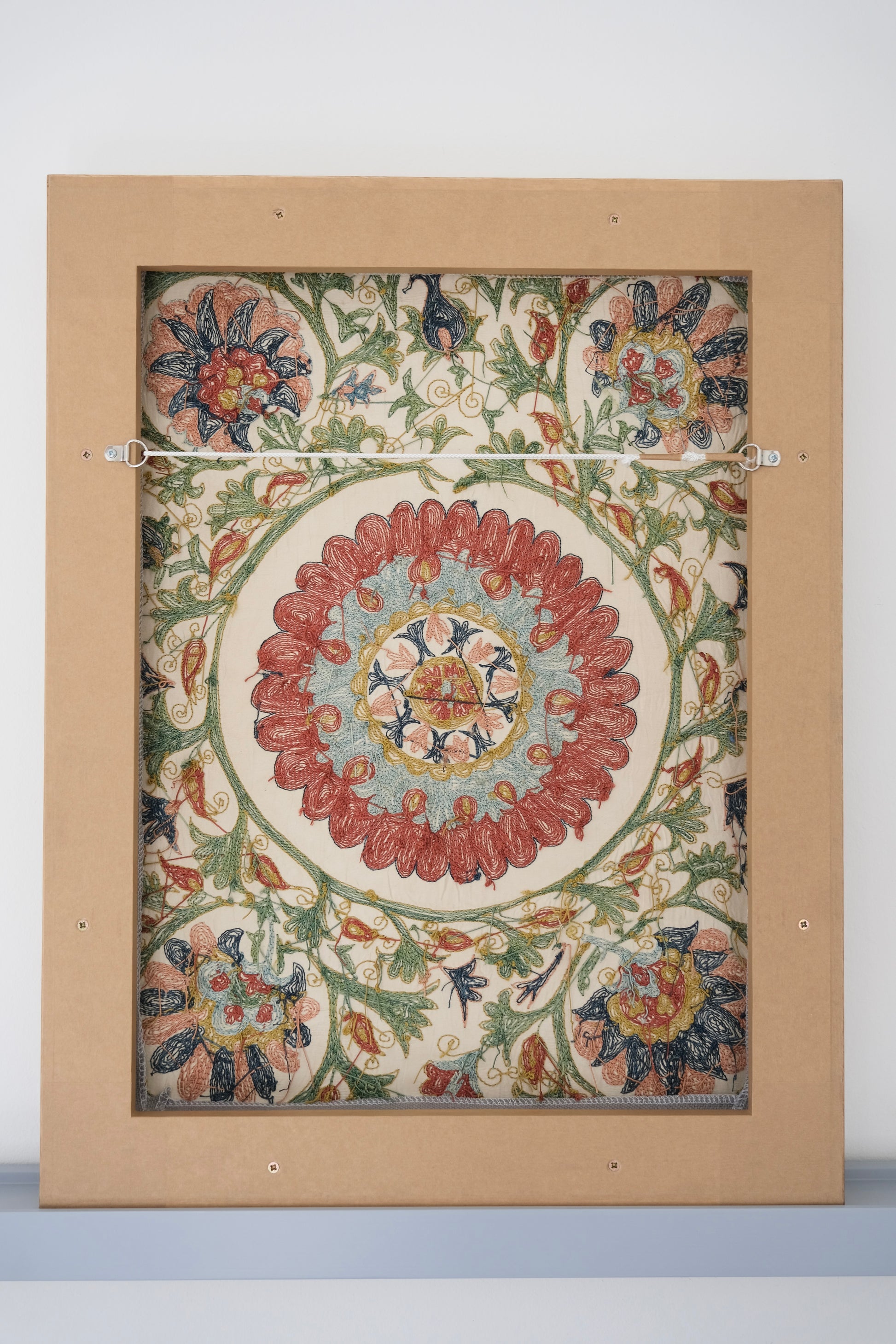 Framed suzani, embroidered textile art, wooden frame, white with green, blue and red floral design, backside