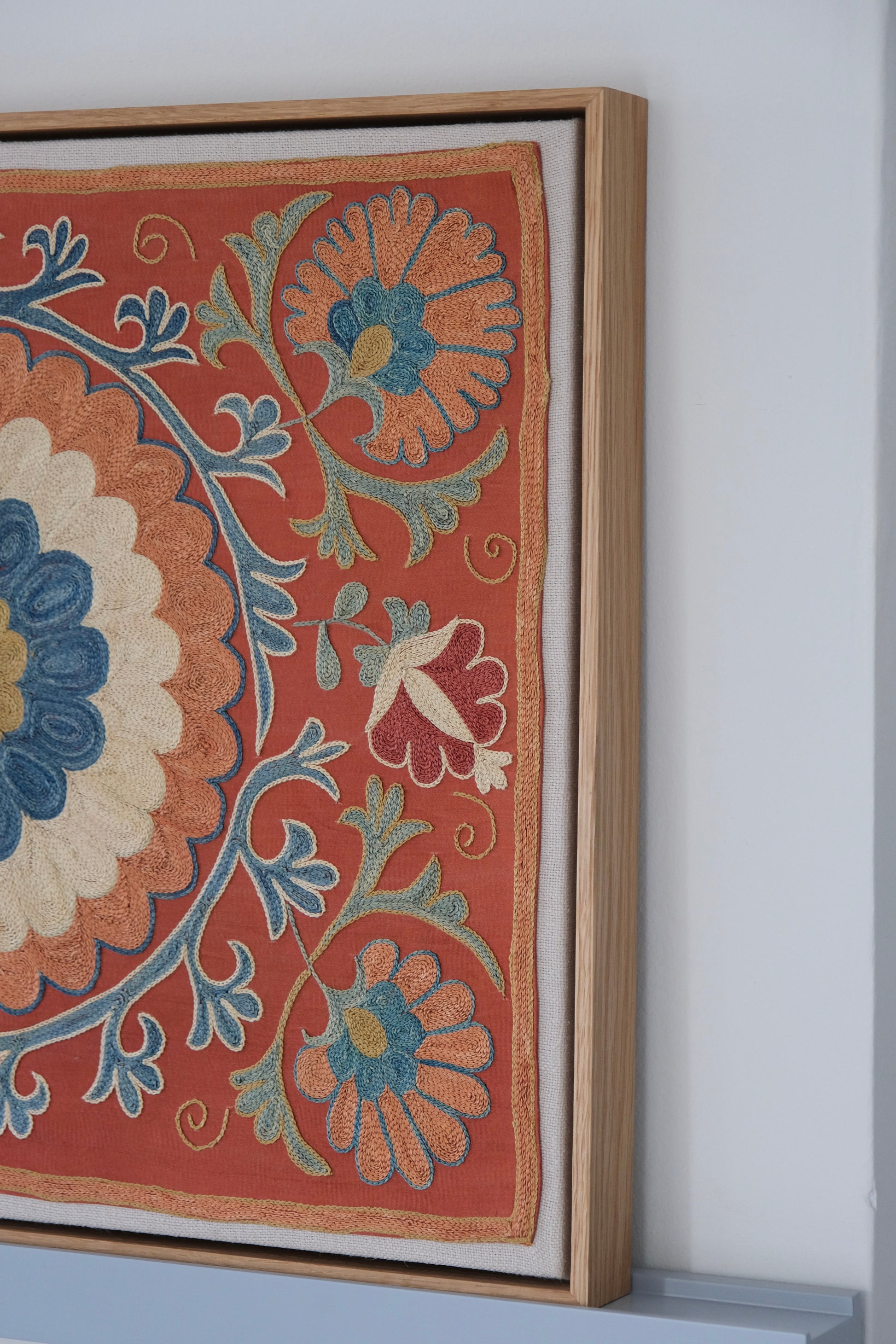 Framed suzani, embroidered textile art, wooden frame, dark orange with blue and green floral motifs, side view
