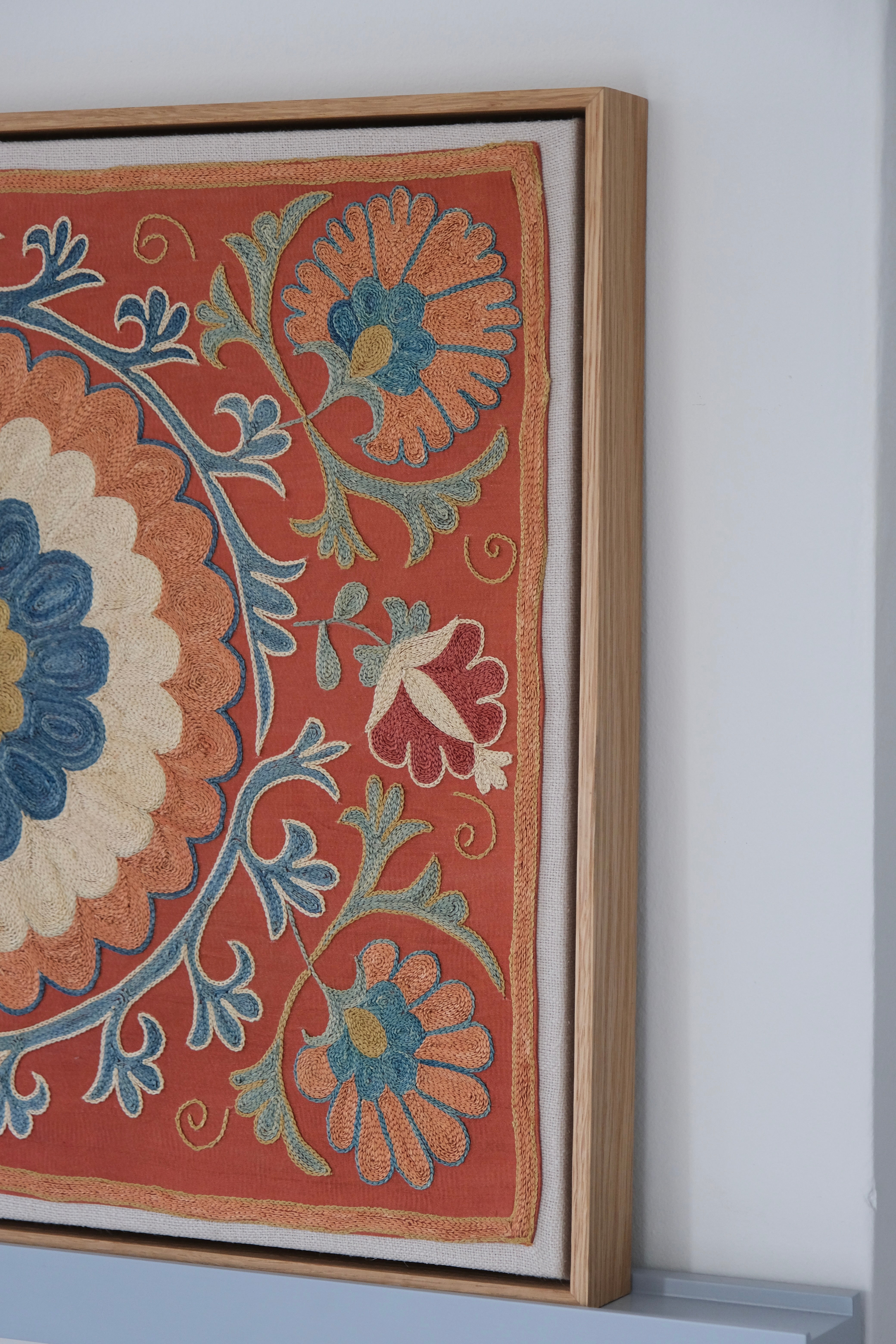 Framed suzani, embroidered textile art, wooden frame, dark orange with blue and green floral motifs, side view